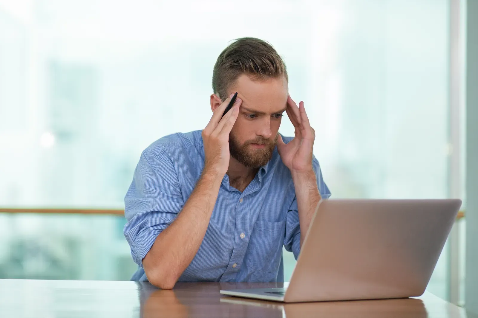 Stressed man holding his head and phone while staring at a laptop, frustrated by data reappearing online