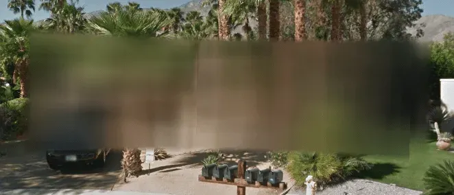 Google Street View of a home blurred out behind palm trees, with driveway, car and mailboxes