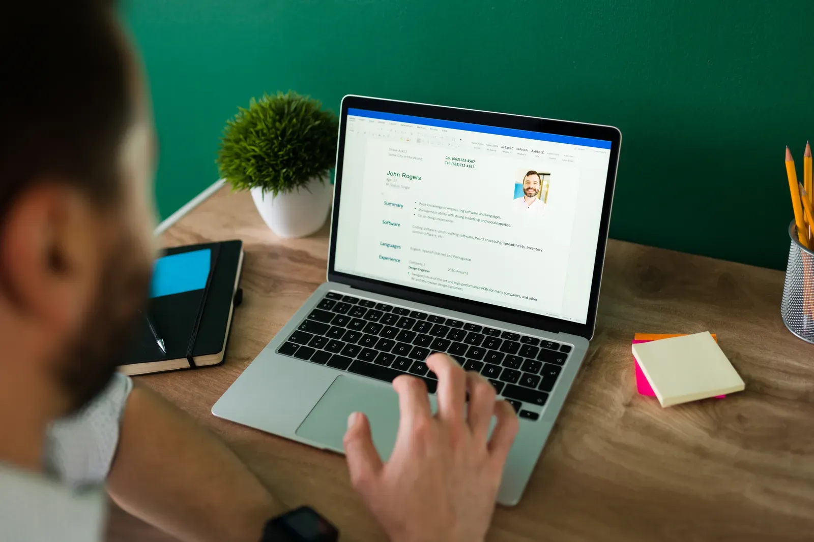 Person editing a resume with personal details on a laptop at a wooden desk