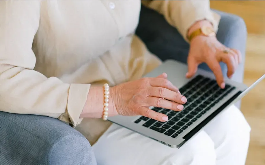 Older woman's hands typing on a laptop while seated