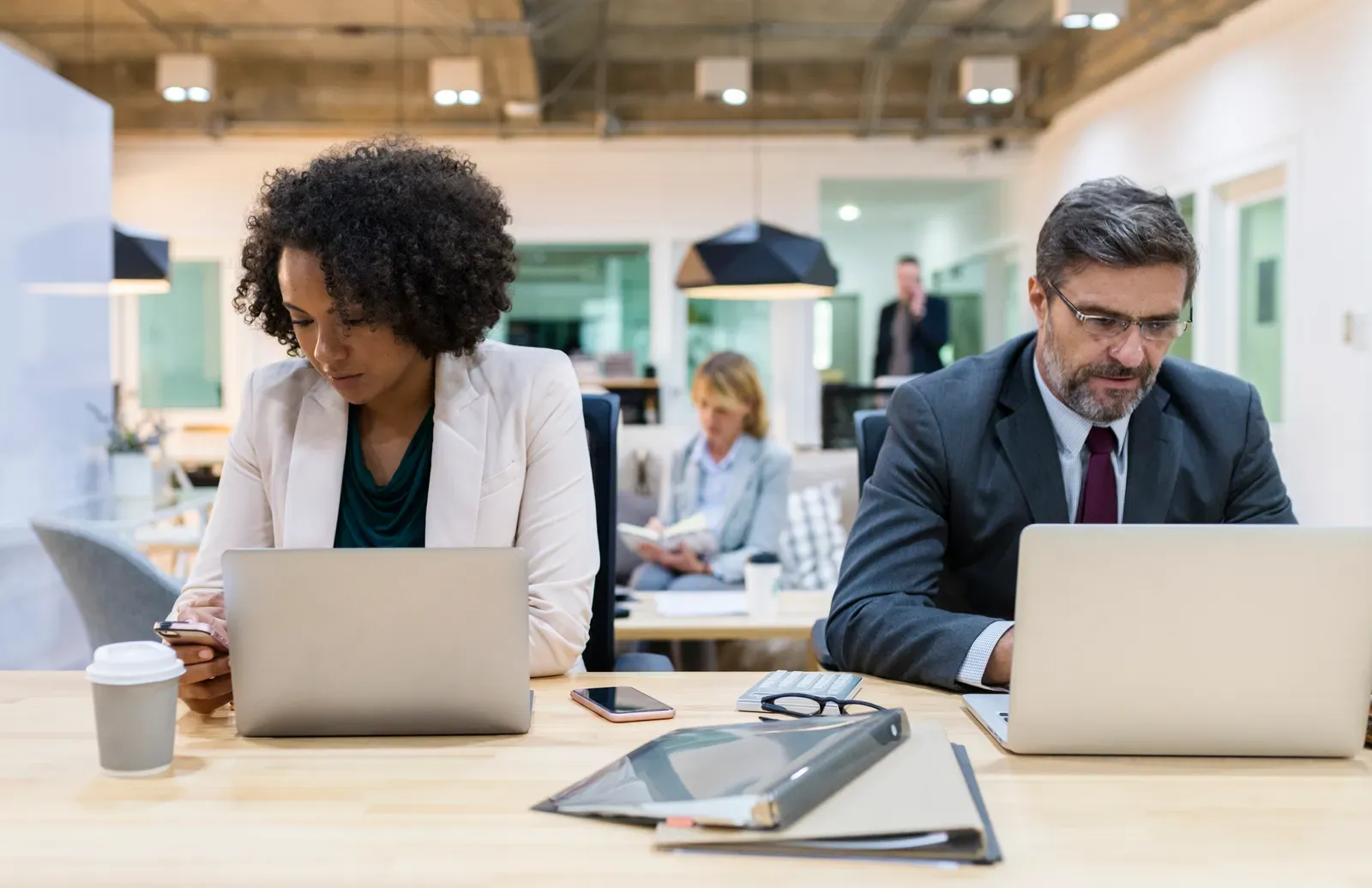 Two business professionals working on laptops at an office table
