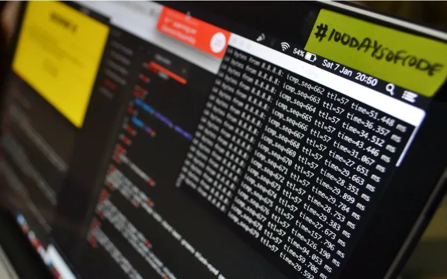 Laptop screen showing scrolling terminal command output beside a #100DaysOfCode sticky note