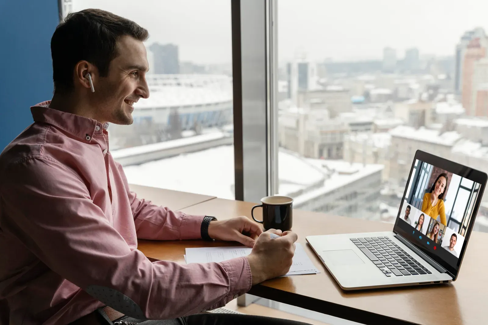 Remote worker on a laptop video call by a high-rise window overlooking a snowy city