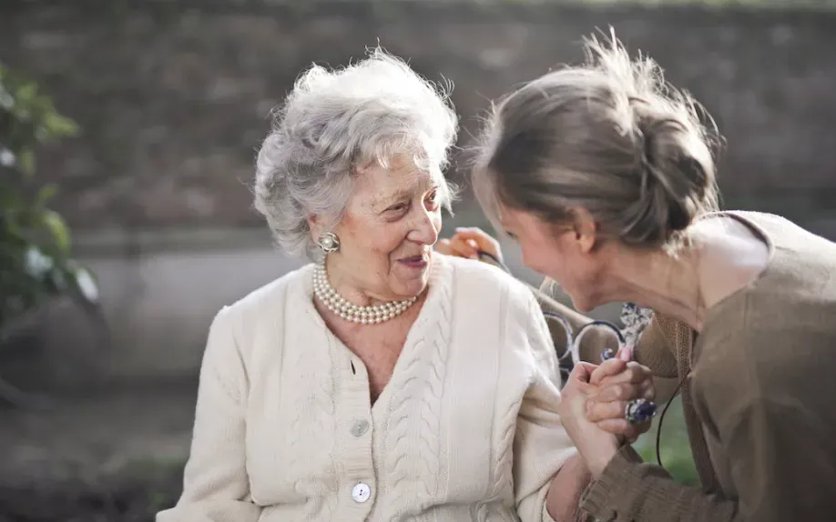 Smiling senior woman talking warmly with a younger woman leaning in beside her outdoors