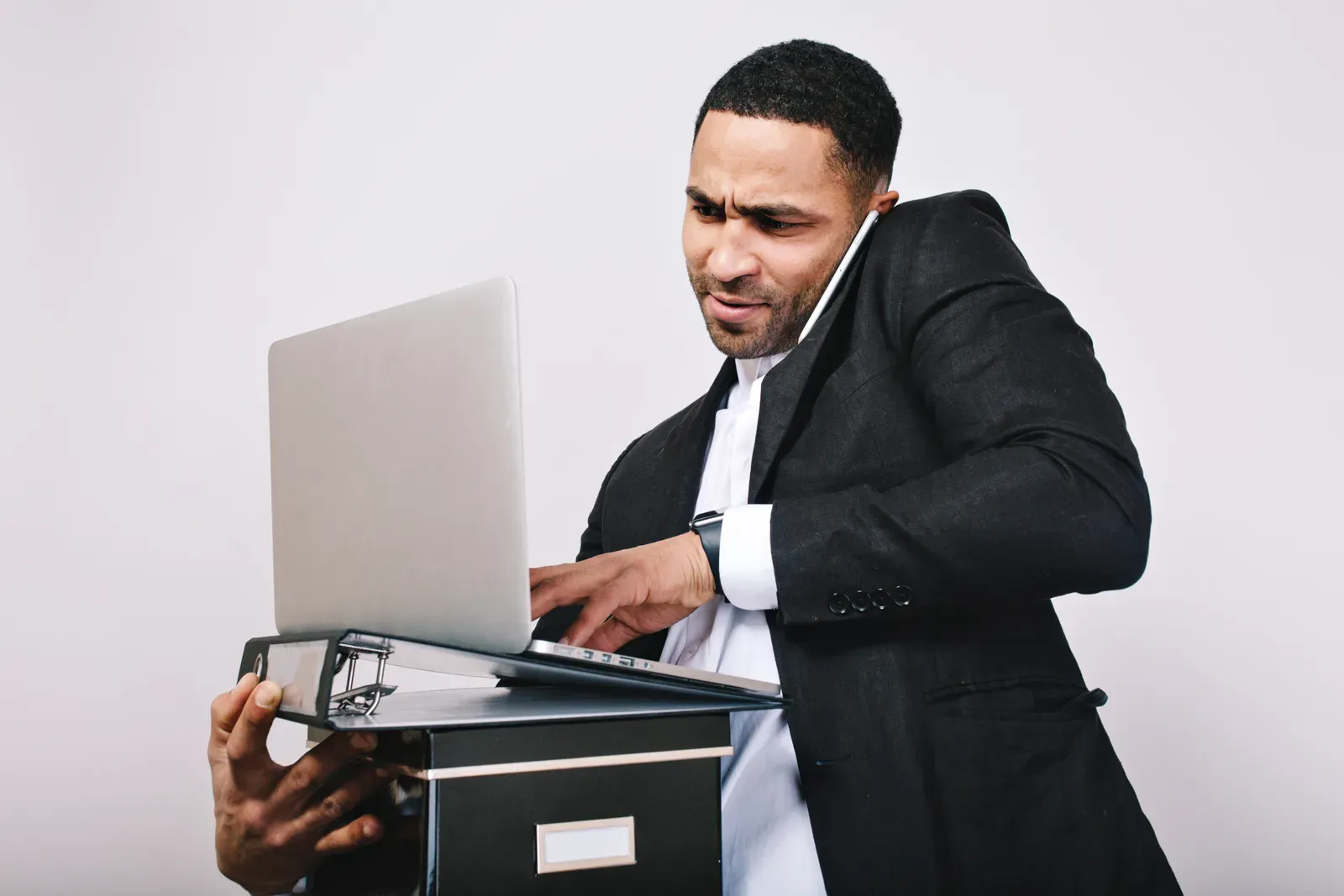 Frustrated businessman on a phone call balancing a laptop on a binder while typing