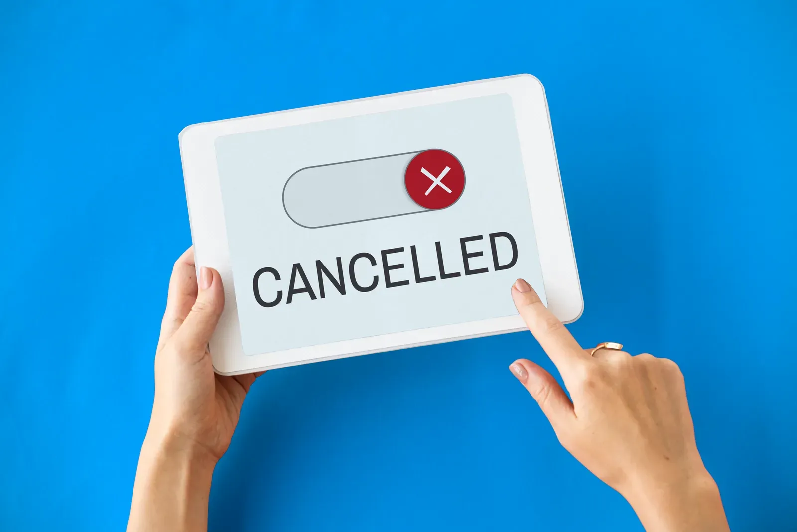 Hands holding a tablet showing a toggle switch and the word Cancelled with a red X