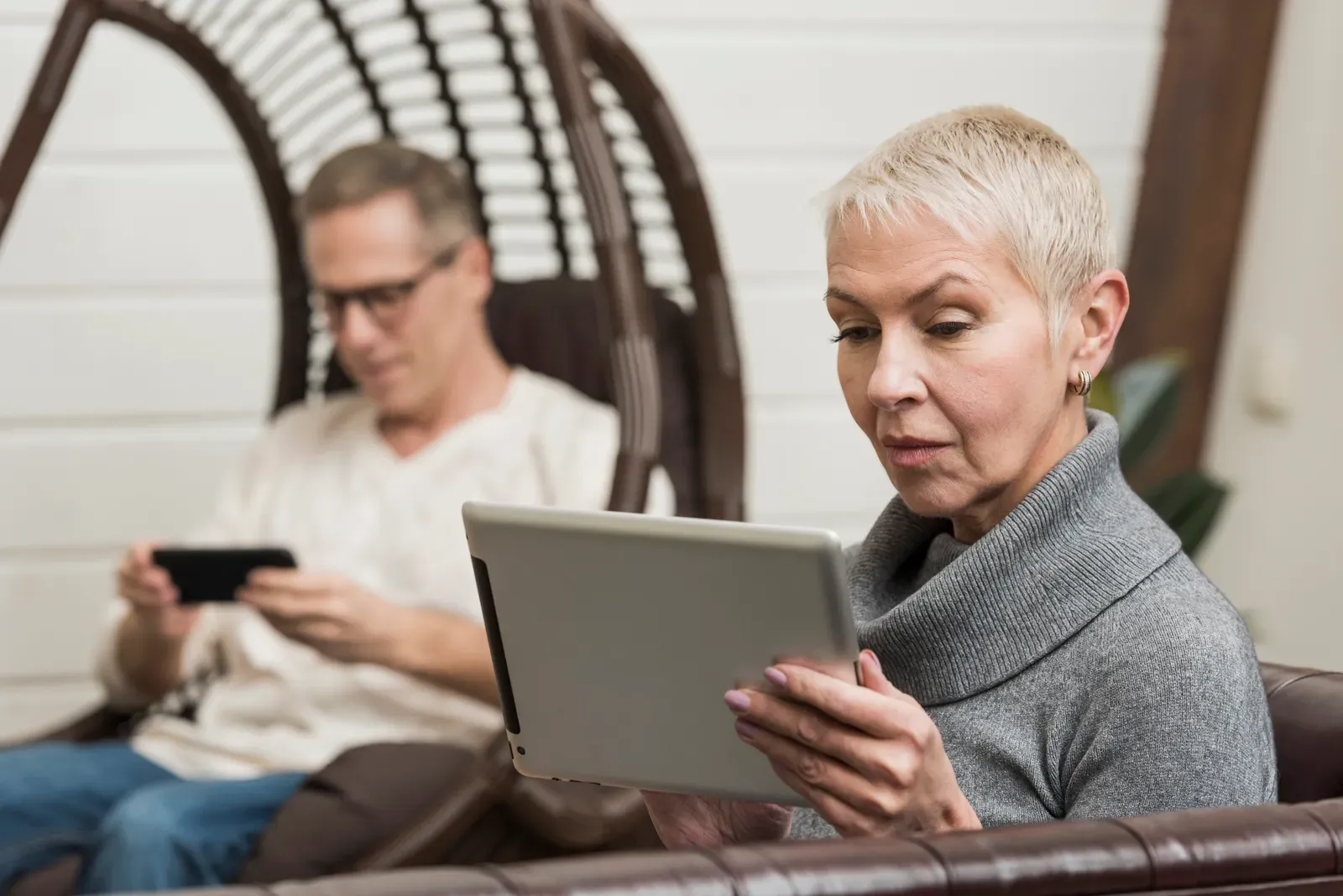 Woman reading on a tablet while a man browses a phone on a porch swing