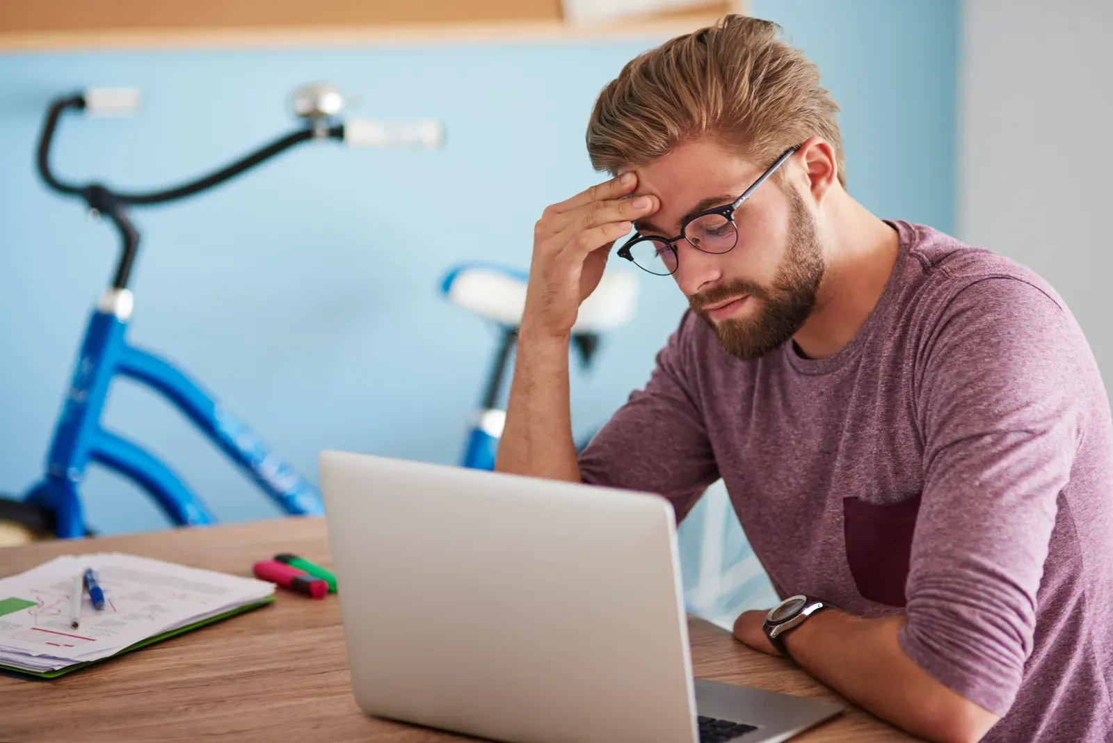 Frustrated man with glasses rubbing his forehead while looking at a laptop