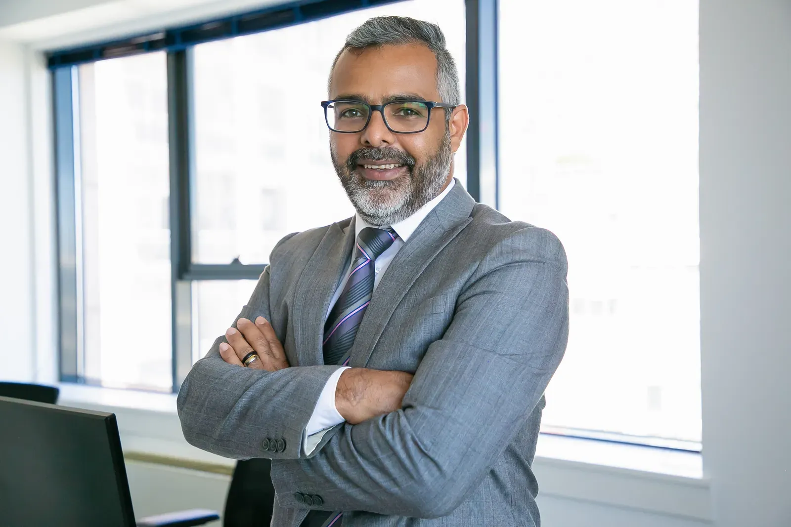 Confident executive in a gray suit and glasses standing arms crossed in an office